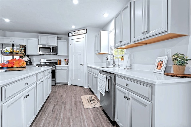 kitchen with light wood-style floors, appliances with stainless steel finishes, light countertops, and a sink