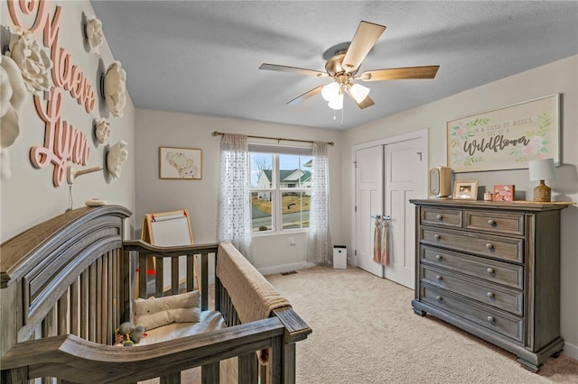 bedroom with a closet, light colored carpet, ceiling fan, a textured ceiling, and baseboards