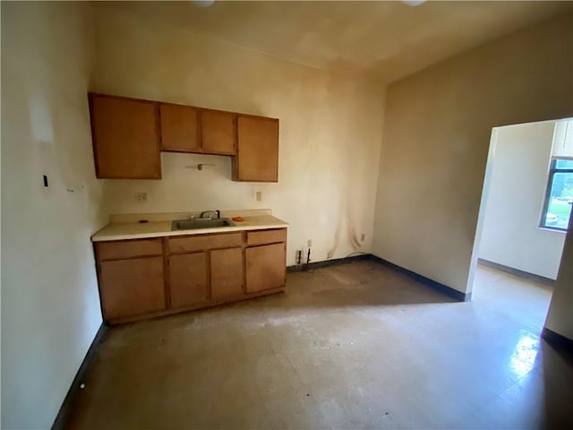 kitchen with a sink, brown cabinets, light countertops, and baseboards
