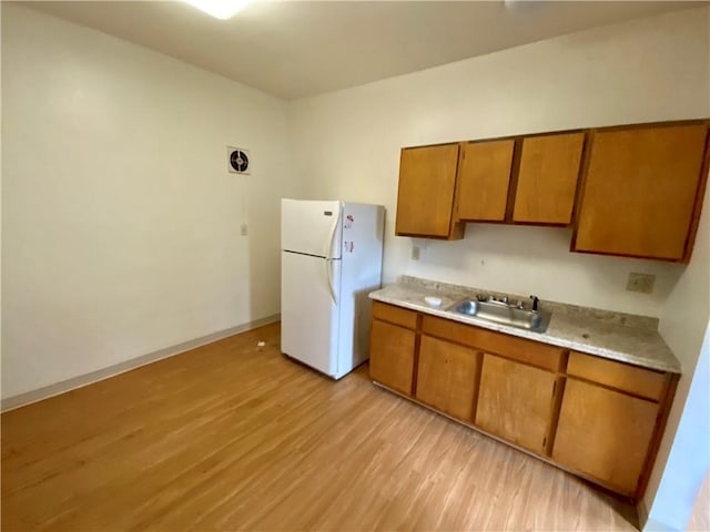 kitchen with freestanding refrigerator, brown cabinetry, light wood-style flooring, and a sink
