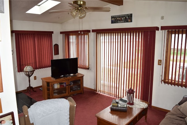 living room featuring dark colored carpet, ceiling fan, and vaulted ceiling with skylight