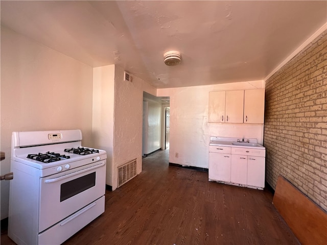 kitchen featuring white range with gas stovetop, brick wall, white cabinetry, and dark hardwood / wood-style floors