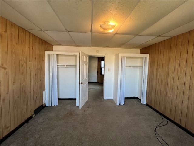 unfurnished bedroom with a drop ceiling, wooden walls, and dark colored carpet