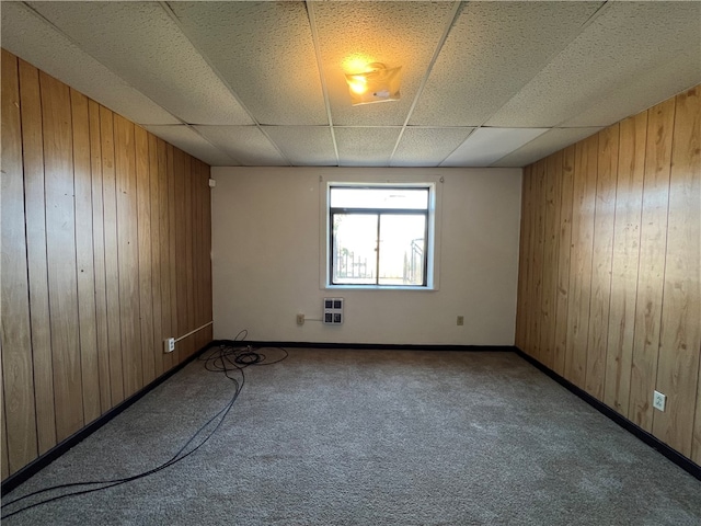 unfurnished room with a drop ceiling, wood walls, and carpet flooring