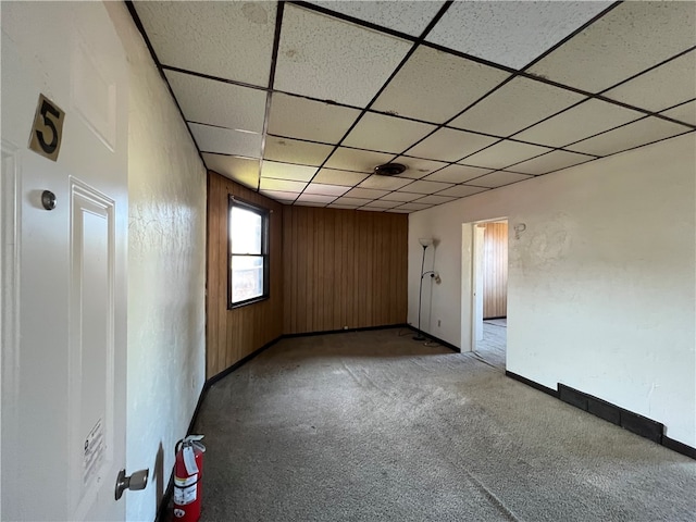 empty room with wooden walls, a drop ceiling, and carpet