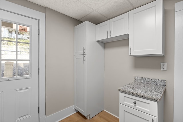 kitchen featuring light stone countertops, a drop ceiling, light wood-type flooring, and white cabinetry