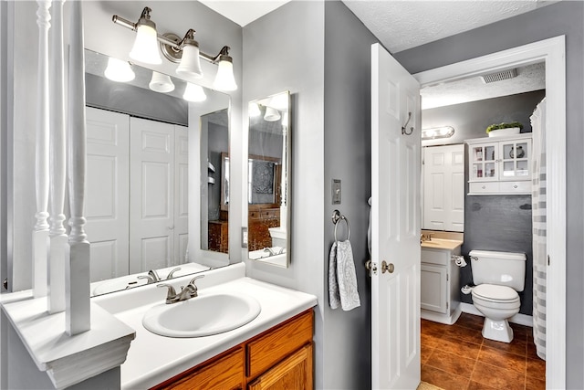 bathroom with vanity, toilet, a textured ceiling, and tile patterned floors