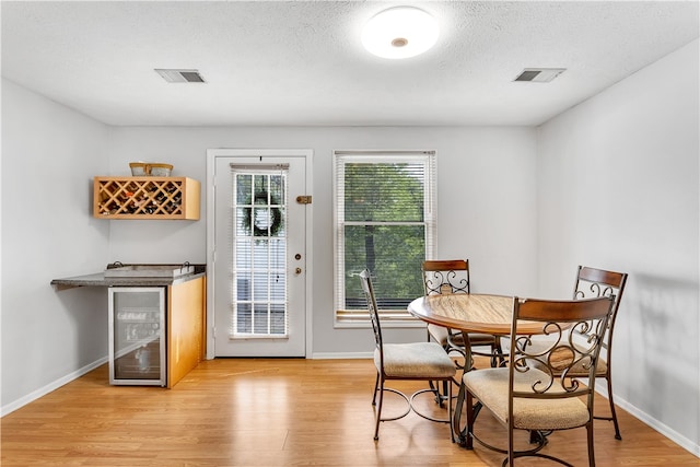 dining area featuring wine cooler, light hardwood / wood-style floors, and a textured ceiling