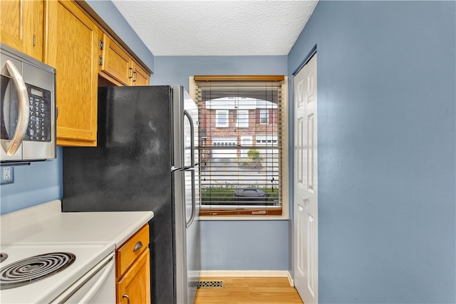 kitchen with appliances with stainless steel finishes, light hardwood / wood-style flooring, and a textured ceiling