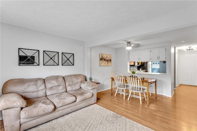 living room featuring light wood-type flooring, ceiling fan, and a textured ceiling