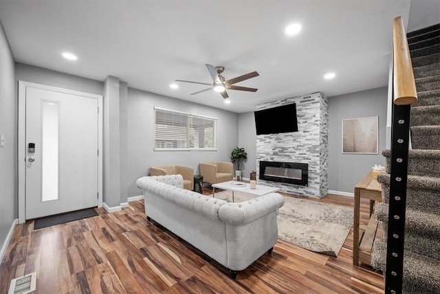 living room featuring ceiling fan, a stone fireplace, and hardwood / wood-style floors