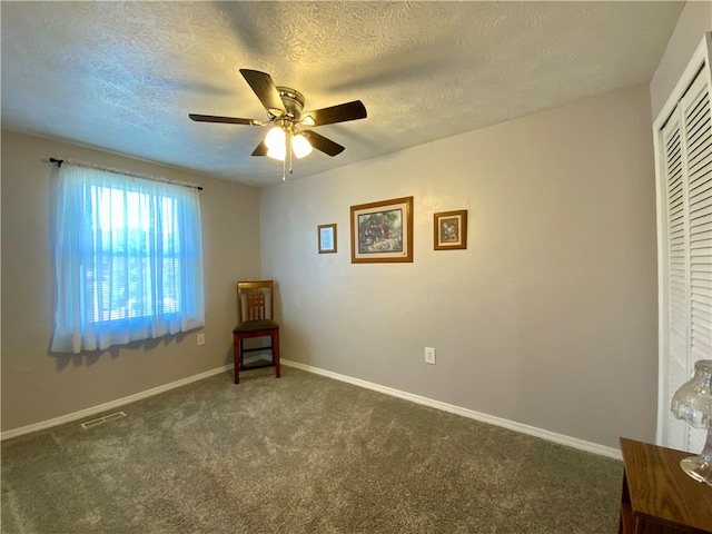 unfurnished room with ceiling fan, a textured ceiling, and dark carpet