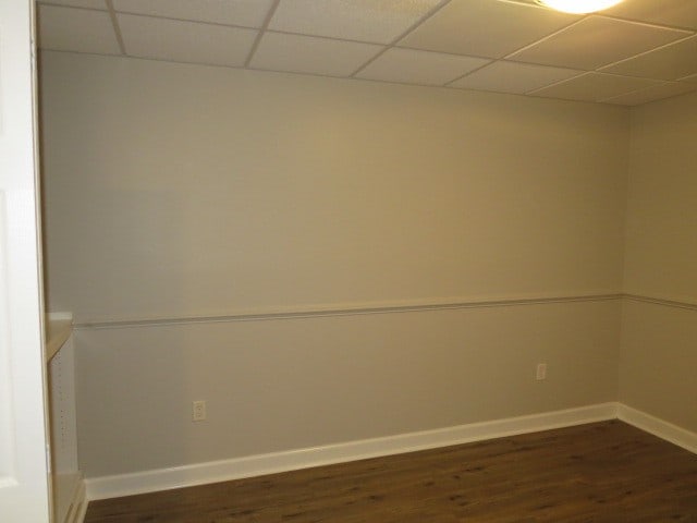 spare room with a paneled ceiling and dark hardwood / wood-style flooring