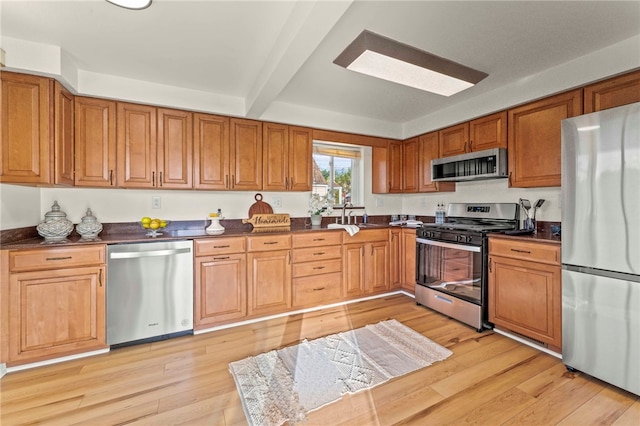 kitchen featuring appliances with stainless steel finishes, beamed ceiling, sink, and light hardwood / wood-style floors