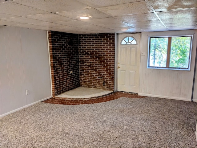 basement featuring a drop ceiling, wooden walls, carpet, and brick wall