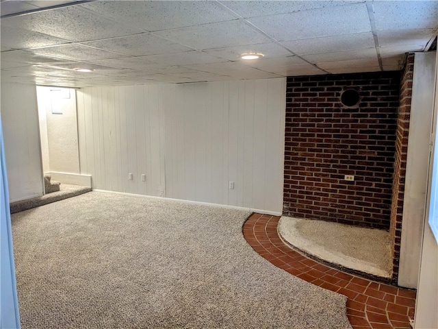 basement featuring dark carpet, a drop ceiling, and wood walls