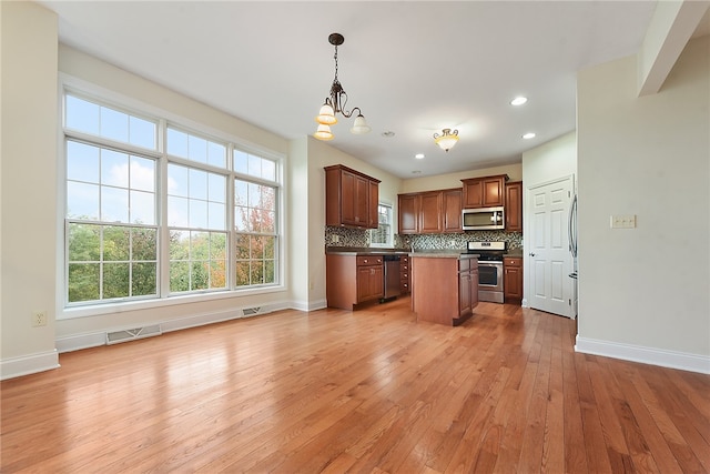 kitchen with appliances with stainless steel finishes, light wood-type flooring, a kitchen island, decorative light fixtures, and a chandelier