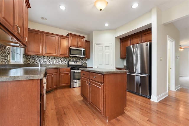 kitchen featuring ceiling fan, appliances with stainless steel finishes, backsplash, a kitchen island, and light hardwood / wood-style floors