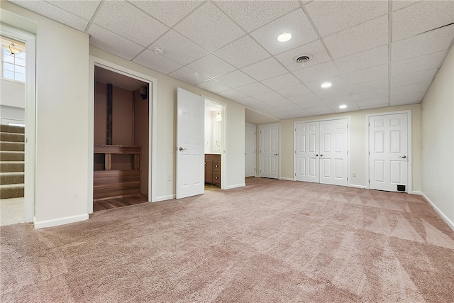 unfurnished bedroom with ensuite bath, carpet floors, a drop ceiling, and two closets