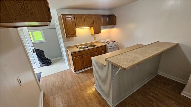 kitchen with white stove, a kitchen breakfast bar, sink, hardwood / wood-style flooring, and exhaust hood