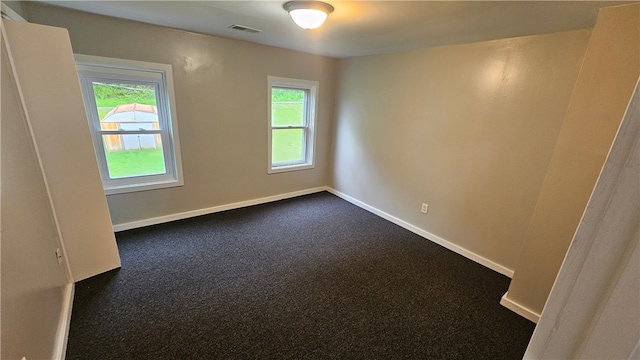 empty room featuring plenty of natural light and dark colored carpet