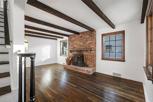 unfurnished living room with a brick fireplace, beamed ceiling, and dark wood-type flooring