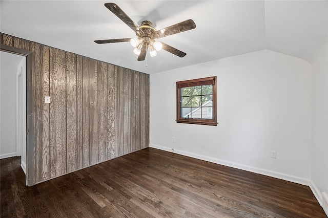 empty room featuring lofted ceiling, dark hardwood / wood-style floors, wooden walls, and ceiling fan