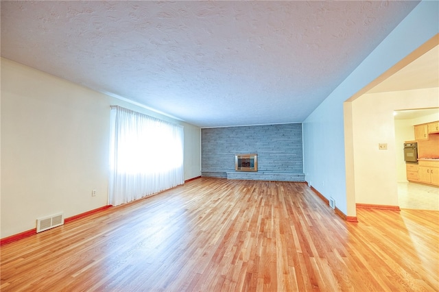 unfurnished living room featuring brick wall, light hardwood / wood-style flooring, a fireplace, and a textured ceiling