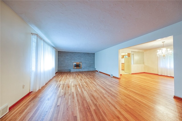 unfurnished living room with a large fireplace, a chandelier, hardwood / wood-style flooring, and a textured ceiling