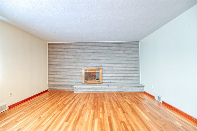 unfurnished living room with light hardwood / wood-style floors, a textured ceiling, brick wall, and a fireplace