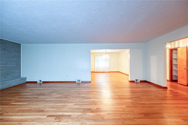 spare room with a large fireplace, a chandelier, a textured ceiling, and light wood-type flooring