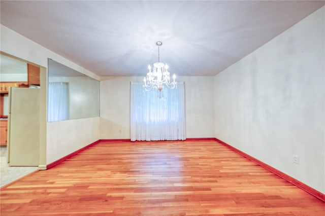 spare room with a chandelier and light wood-type flooring