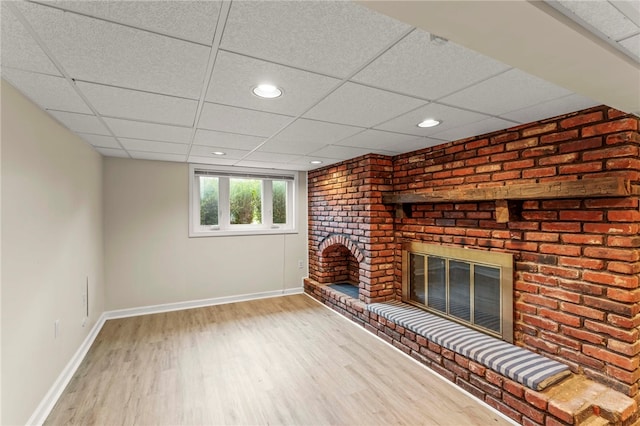 unfurnished living room with brick wall, a fireplace, a drop ceiling, and hardwood / wood-style floors