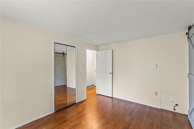 unfurnished bedroom featuring a barn door, hardwood / wood-style floors, and a closet