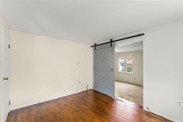 spare room with a barn door and dark wood-type flooring