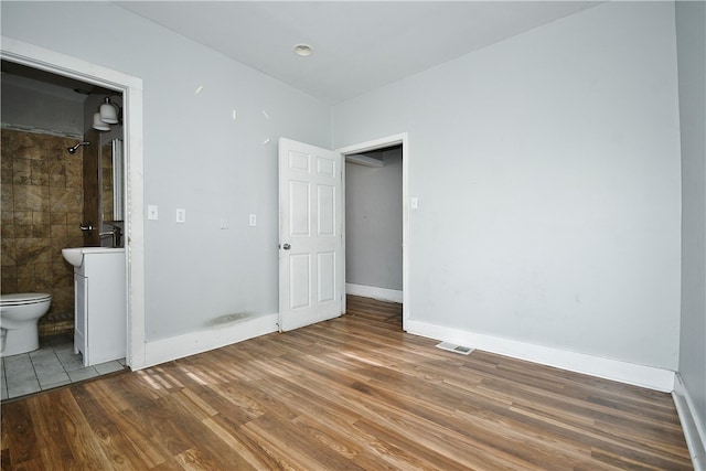 unfurnished bedroom featuring hardwood / wood-style flooring and connected bathroom