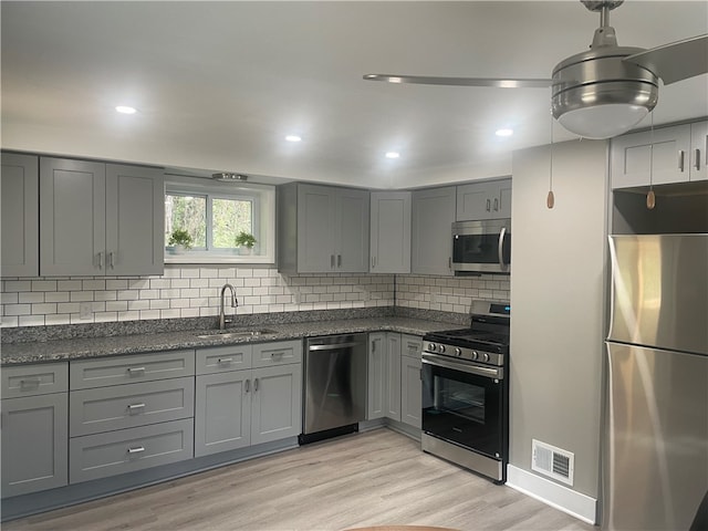 kitchen with stainless steel appliances, tasteful backsplash, gray cabinetry, sink, and light hardwood / wood-style flooring