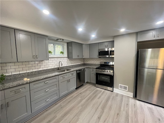 kitchen featuring light wood-type flooring, stainless steel appliances, gray cabinetry, dark stone countertops, and sink