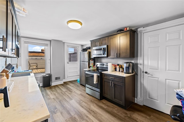 kitchen featuring appliances with stainless steel finishes, dark brown cabinets, light stone countertops, and light hardwood / wood-style flooring