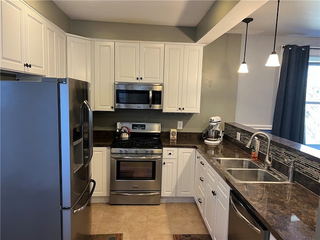 kitchen featuring sink, hanging light fixtures, stainless steel appliances, dark stone counters, and white cabinets