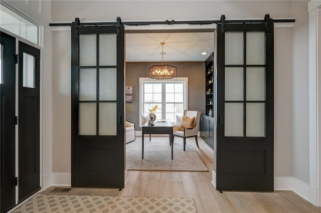 doorway with a notable chandelier, light wood-type flooring, and a barn door