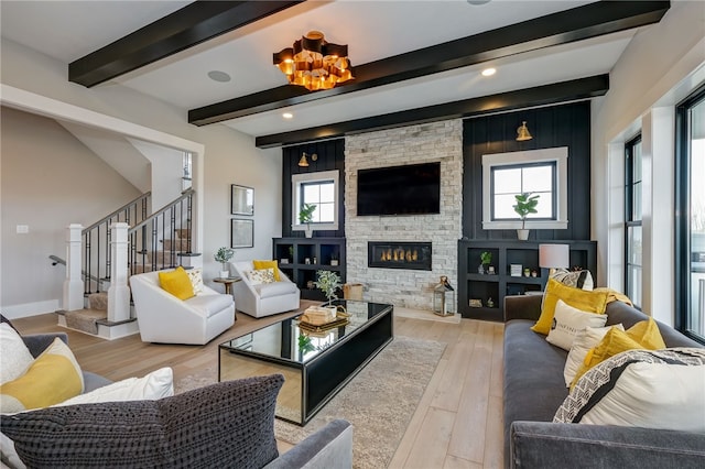 living room with light hardwood / wood-style floors, beam ceiling, and a stone fireplace