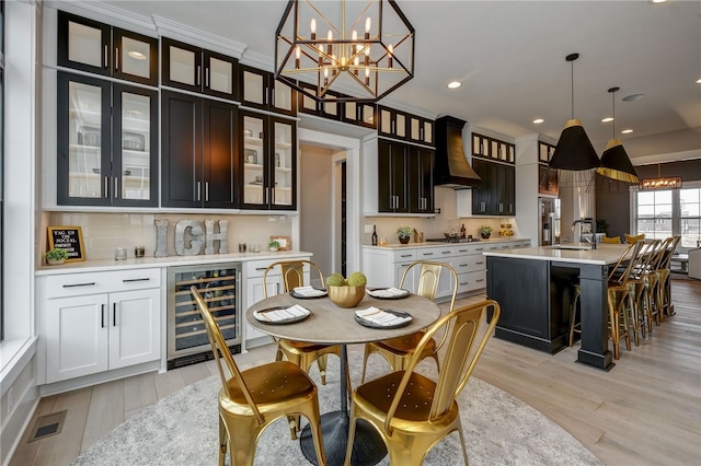 interior space with light wood-type flooring, beverage cooler, sink, a notable chandelier, and crown molding