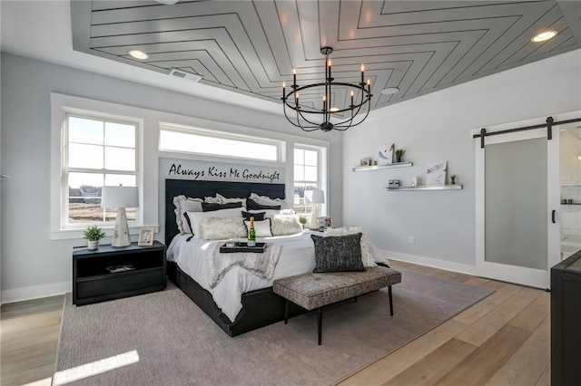 bedroom with a barn door, light hardwood / wood-style floors, an inviting chandelier, wooden ceiling, and ensuite bath