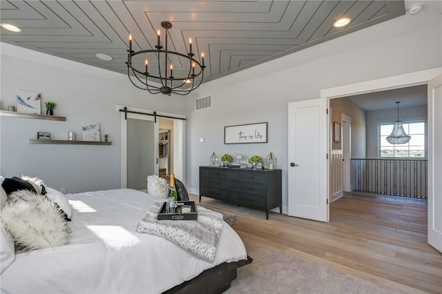 bedroom with a barn door, a notable chandelier, and light hardwood / wood-style flooring