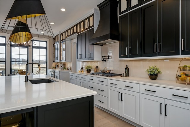 kitchen with custom exhaust hood, sink, white cabinetry, stainless steel gas stovetop, and light hardwood / wood-style floors