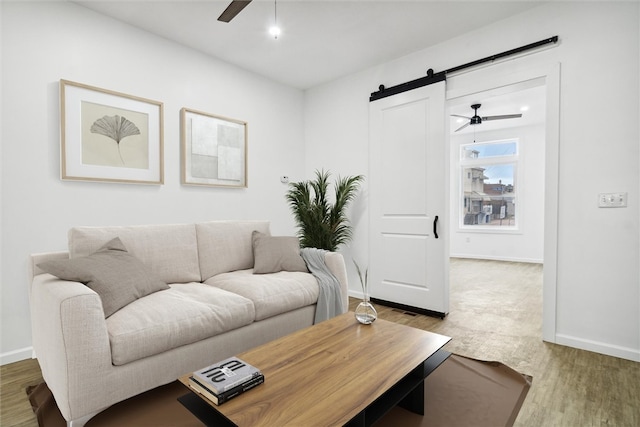 living room with a barn door, light hardwood / wood-style flooring, and ceiling fan