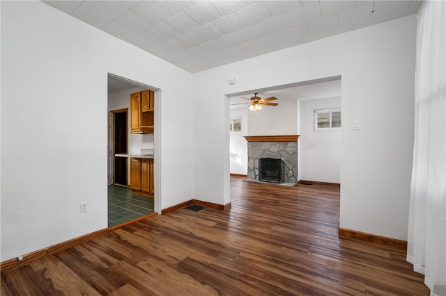 unfurnished living room featuring ceiling fan, a stone fireplace, and dark hardwood / wood-style flooring