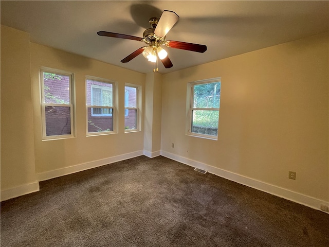 empty room with ceiling fan, dark colored carpet, and a healthy amount of sunlight