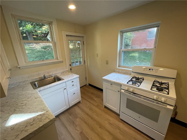 kitchen with light hardwood / wood-style floors, white gas range oven, tasteful backsplash, sink, and white cabinetry